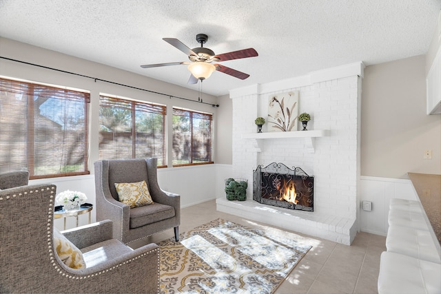 living room featuring ceiling fan, light tile patterned floors, a textured ceiling, and a brick fireplace