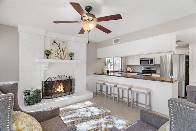 tiled living room featuring a fireplace, a textured ceiling, ceiling fan, and sink