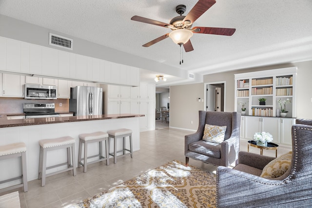 living room featuring ceiling fan, light tile patterned flooring, and a textured ceiling