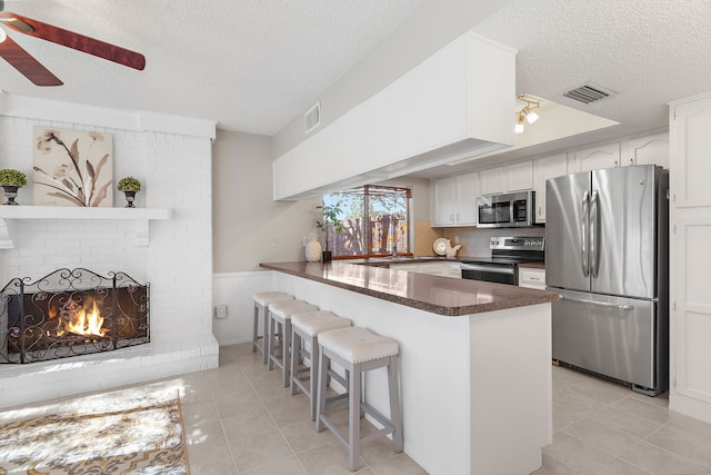 kitchen with a breakfast bar, a textured ceiling, white cabinetry, kitchen peninsula, and stainless steel appliances