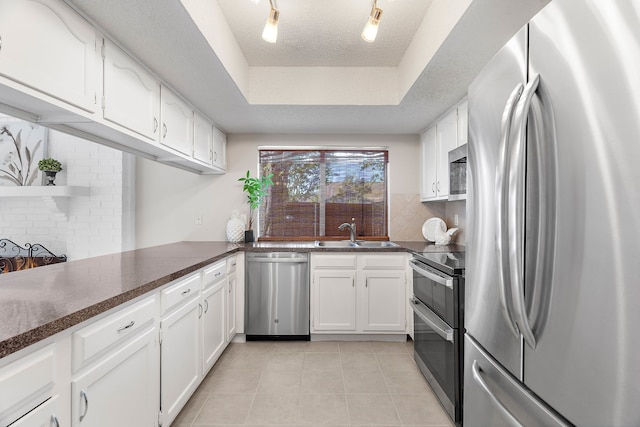 kitchen featuring appliances with stainless steel finishes, a textured ceiling, a tray ceiling, sink, and white cabinets