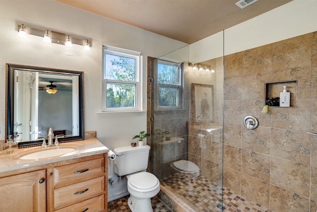 bathroom with a tile shower, vanity, toilet, and ceiling fan