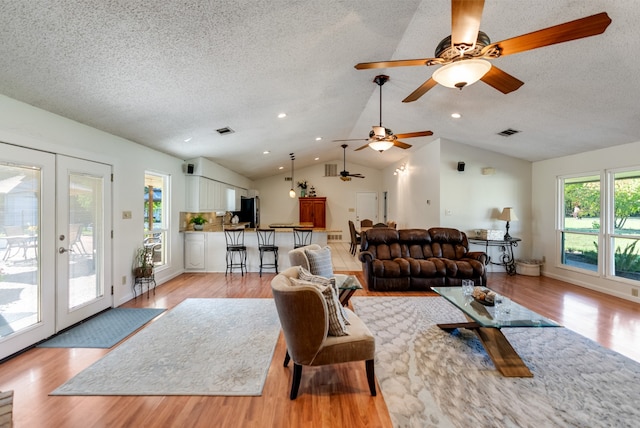 living room with french doors, a textured ceiling, light hardwood / wood-style floors, and lofted ceiling