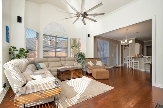 living room with dark hardwood / wood-style flooring, ceiling fan with notable chandelier, ornamental molding, and a high ceiling