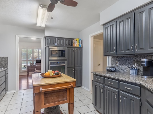 kitchen featuring appliances with stainless steel finishes, tasteful backsplash, dark stone countertops, gray cabinets, and light tile patterned flooring