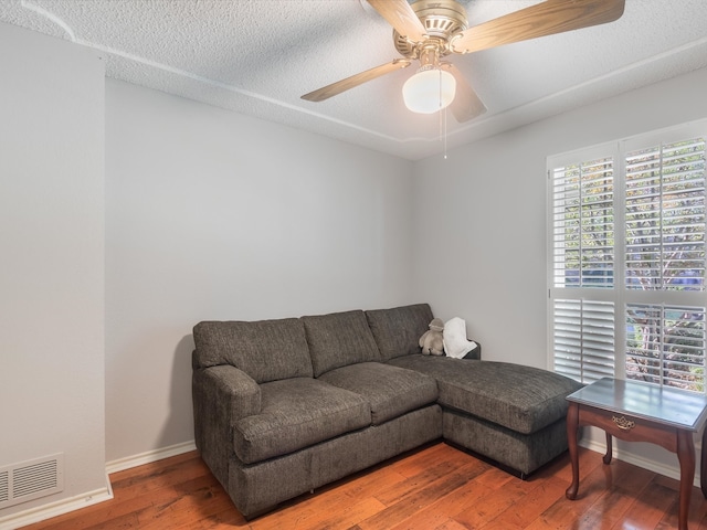 living room with ceiling fan, plenty of natural light, wood-type flooring, and a textured ceiling