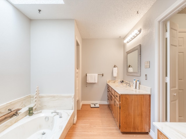 bathroom with vanity, a skylight, a tub to relax in, a textured ceiling, and wood-type flooring