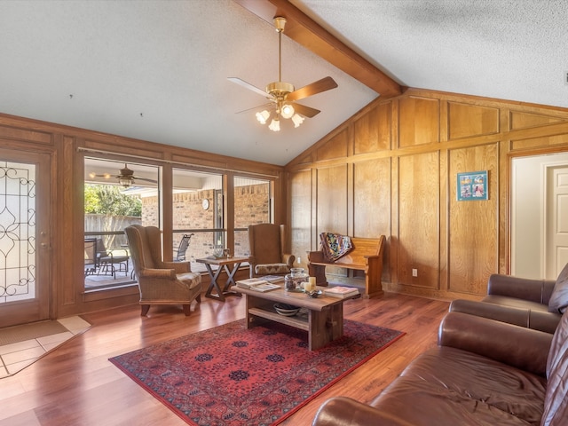 living room with a textured ceiling, ceiling fan, hardwood / wood-style floors, vaulted ceiling with beams, and wood walls