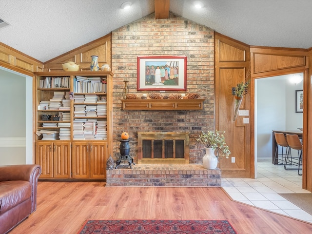 living room featuring light wood-type flooring, a brick fireplace, a textured ceiling, wooden walls, and vaulted ceiling with beams