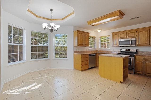 kitchen featuring appliances with stainless steel finishes, a raised ceiling, light tile patterned floors, a notable chandelier, and a center island