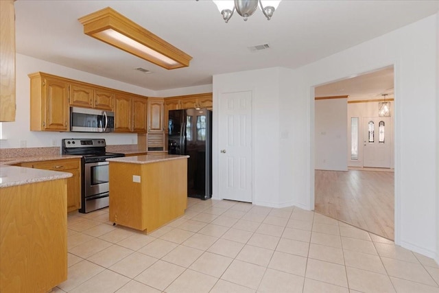 kitchen with a notable chandelier, appliances with stainless steel finishes, a kitchen island, and light tile patterned floors