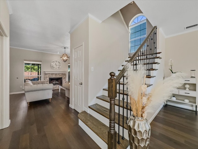 stairway featuring hardwood / wood-style flooring, a stone fireplace, and crown molding