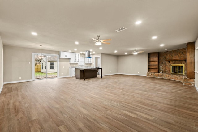 unfurnished living room featuring ceiling fan with notable chandelier, a stone fireplace, and wood-type flooring