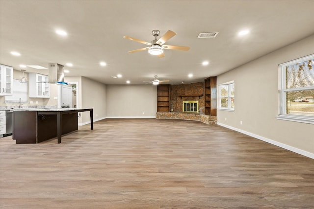 unfurnished living room featuring a stone fireplace, ceiling fan, sink, and light hardwood / wood-style floors