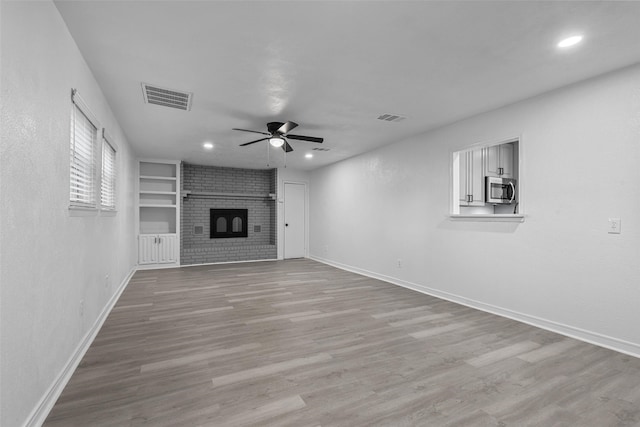 unfurnished living room featuring built in shelves, ceiling fan, a fireplace, and light wood-type flooring