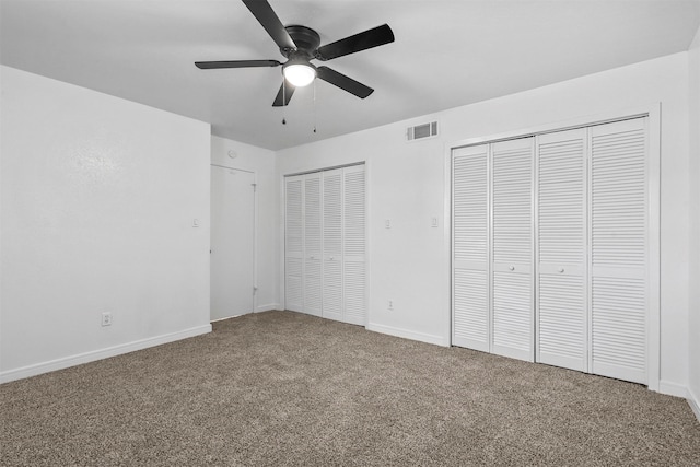 unfurnished bedroom featuring ceiling fan, carpet floors, and multiple closets