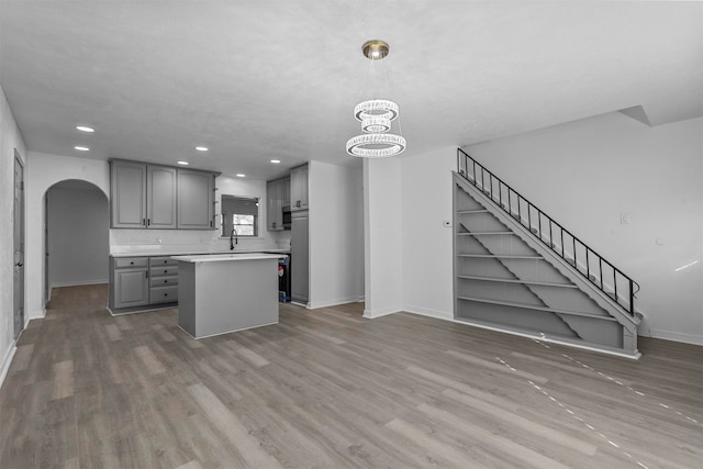 kitchen with gray cabinetry, sink, an inviting chandelier, a center island, and light hardwood / wood-style floors