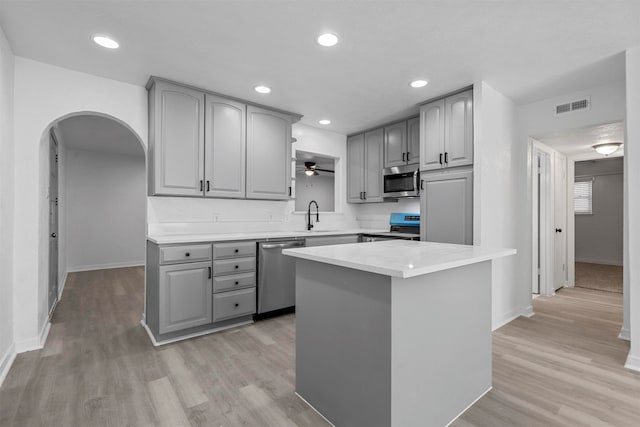 kitchen featuring appliances with stainless steel finishes, light wood-type flooring, sink, a center island, and gray cabinets