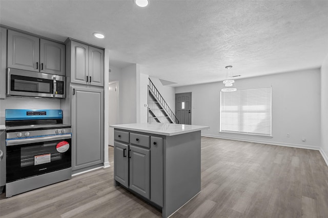 kitchen with hanging light fixtures, light hardwood / wood-style flooring, gray cabinets, a kitchen island, and stainless steel appliances