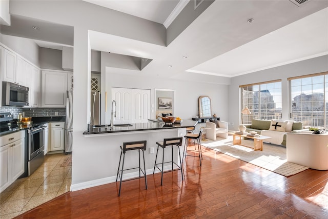 kitchen featuring backsplash, sink, appliances with stainless steel finishes, a kitchen bar, and white cabinetry