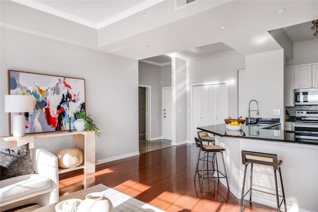 interior space featuring stainless steel appliances, crown molding, sink, white cabinets, and a breakfast bar area