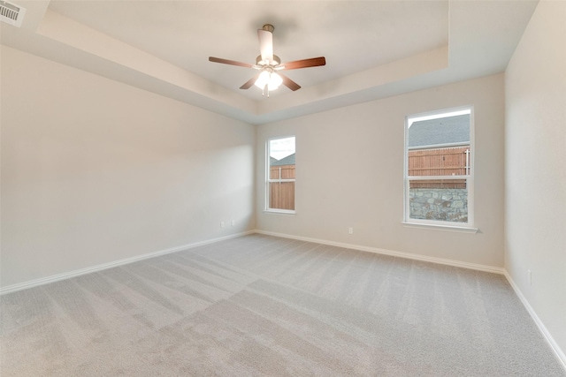 empty room featuring a tray ceiling, light colored carpet, and ceiling fan