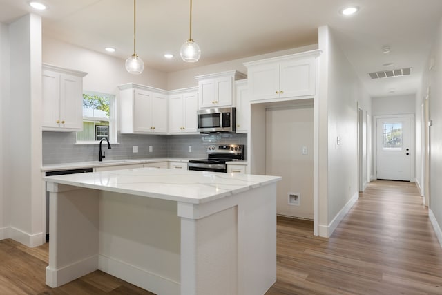 kitchen with light stone countertops, appliances with stainless steel finishes, white cabinets, a kitchen island, and hanging light fixtures