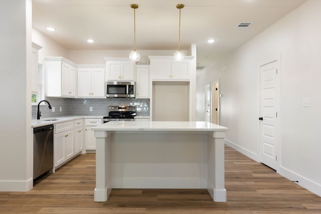 kitchen with a center island, hanging light fixtures, hardwood / wood-style flooring, white cabinetry, and stainless steel appliances