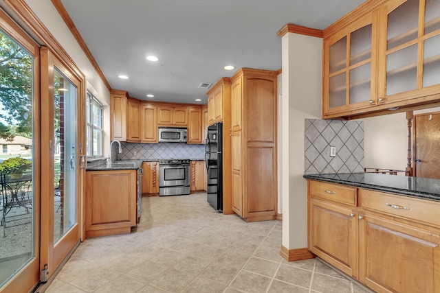 kitchen with plenty of natural light, dark stone countertops, ornamental molding, and stainless steel appliances