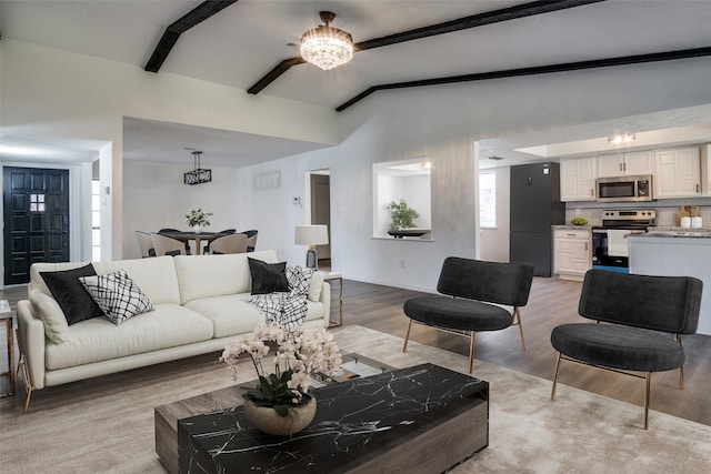 living room featuring vaulted ceiling with beams, a chandelier, and light hardwood / wood-style flooring