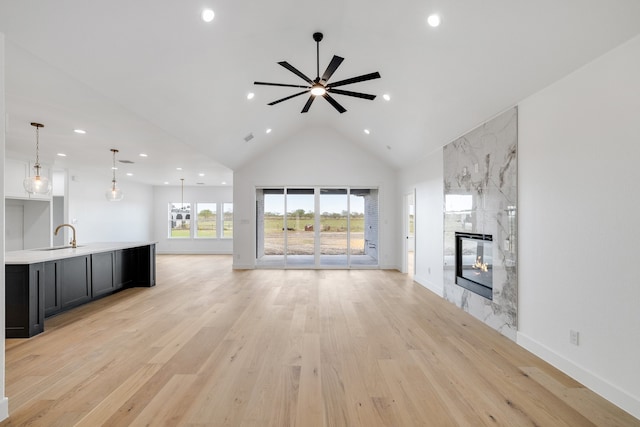 unfurnished living room featuring ceiling fan, sink, a high end fireplace, high vaulted ceiling, and light hardwood / wood-style floors