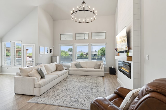 living room with a fireplace, light hardwood / wood-style floors, high vaulted ceiling, and a chandelier