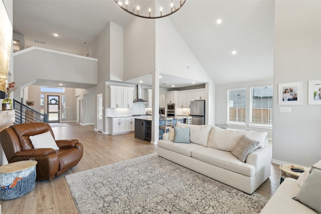 living room featuring a chandelier, high vaulted ceiling, a healthy amount of sunlight, and light hardwood / wood-style floors