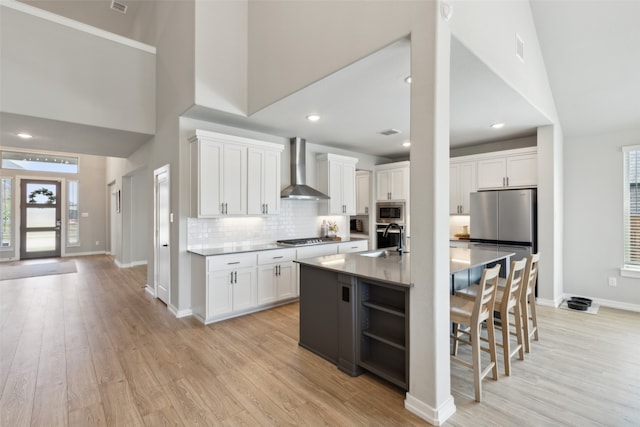 kitchen featuring white cabinets, wall chimney exhaust hood, an island with sink, and light hardwood / wood-style floors