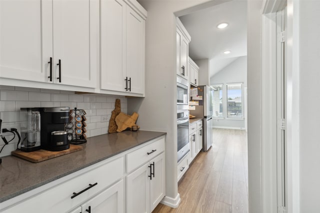 kitchen featuring white cabinets, light hardwood / wood-style floors, dark stone countertops, and tasteful backsplash