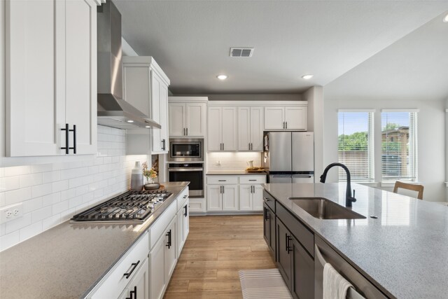 kitchen featuring white cabinetry, sink, wall chimney exhaust hood, stainless steel appliances, and light hardwood / wood-style floors