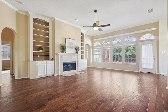 unfurnished living room with ornamental molding, built in shelves, a textured ceiling, ceiling fan, and dark hardwood / wood-style floors