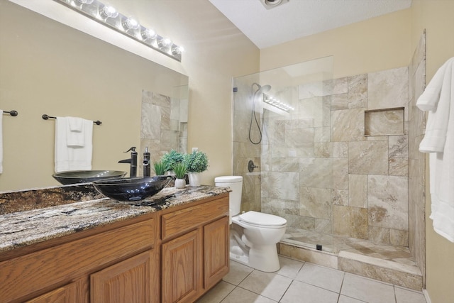 bathroom with vanity, tile patterned flooring, toilet, a textured ceiling, and a tile shower