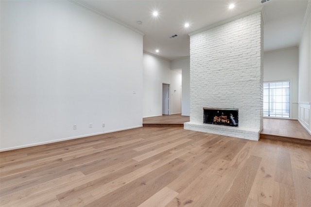 unfurnished living room featuring a stone fireplace, ornamental molding, and light wood-type flooring