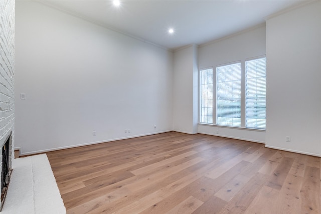 spare room with light wood-type flooring, ornamental molding, a brick fireplace, and baseboards