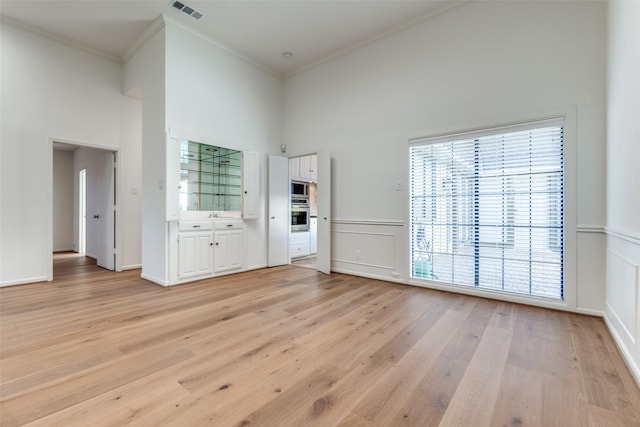 interior space with light wood-style flooring, visible vents, crown molding, and a towering ceiling