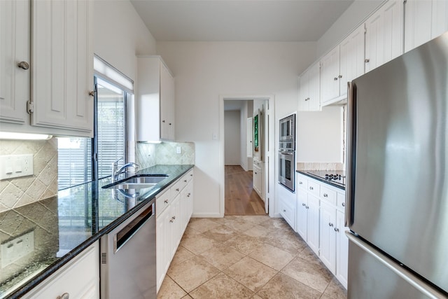 kitchen featuring tasteful backsplash, dark stone counters, stainless steel appliances, white cabinetry, and a sink