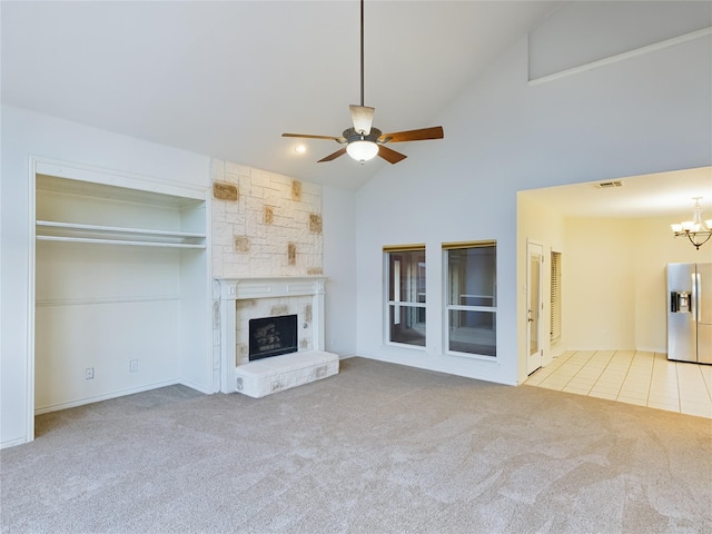 unfurnished living room with light carpet, a stone fireplace, ceiling fan with notable chandelier, and high vaulted ceiling