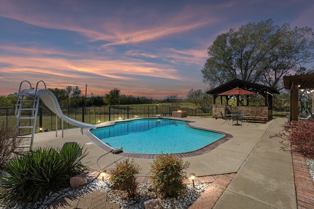 pool at dusk with a gazebo, a patio area, and a water slide