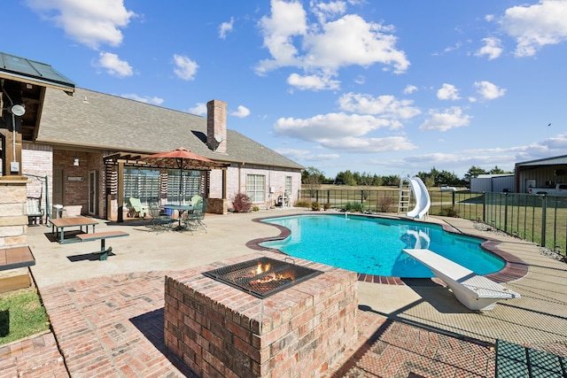 view of swimming pool featuring a patio, a diving board, an outdoor fire pit, and a water slide