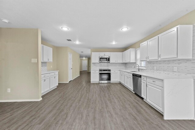 kitchen with backsplash, white cabinets, stainless steel appliances, and light wood-type flooring