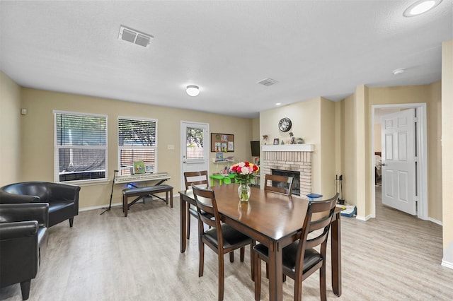 dining room with light hardwood / wood-style flooring, a textured ceiling, and a brick fireplace