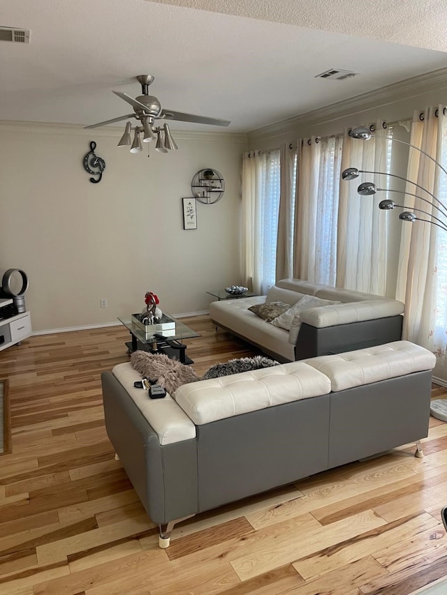 living room featuring ceiling fan, light hardwood / wood-style flooring, a textured ceiling, and ornamental molding