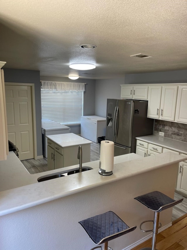 kitchen with light wood-type flooring, a kitchen island, sink, stainless steel fridge with ice dispenser, and white cabinetry