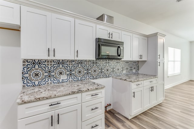 kitchen featuring white cabinets, decorative backsplash, light stone counters, and light wood-type flooring